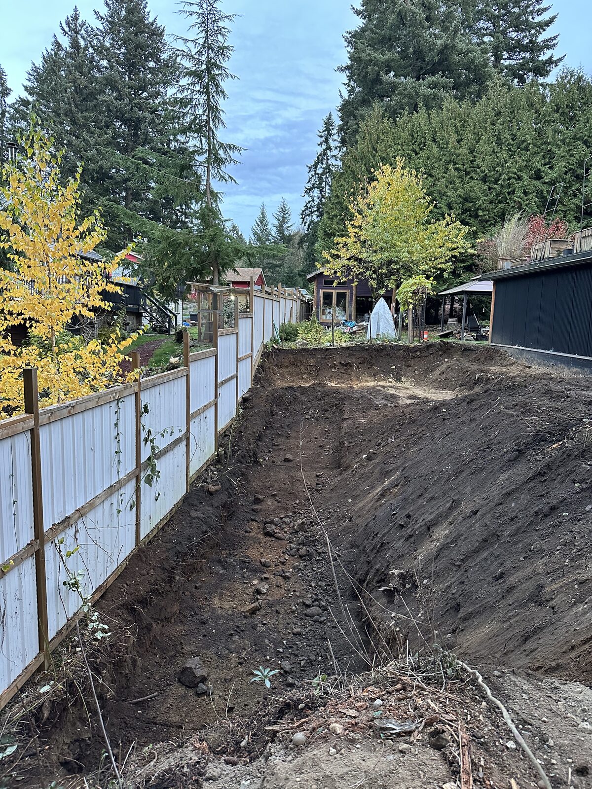 Initial clearing and excavation along the property fence — garage addition and house underpinning project