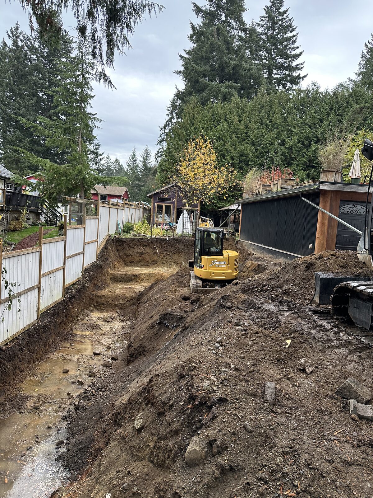 Compact excavator working beside the existing house — garage addition and house underpinning project