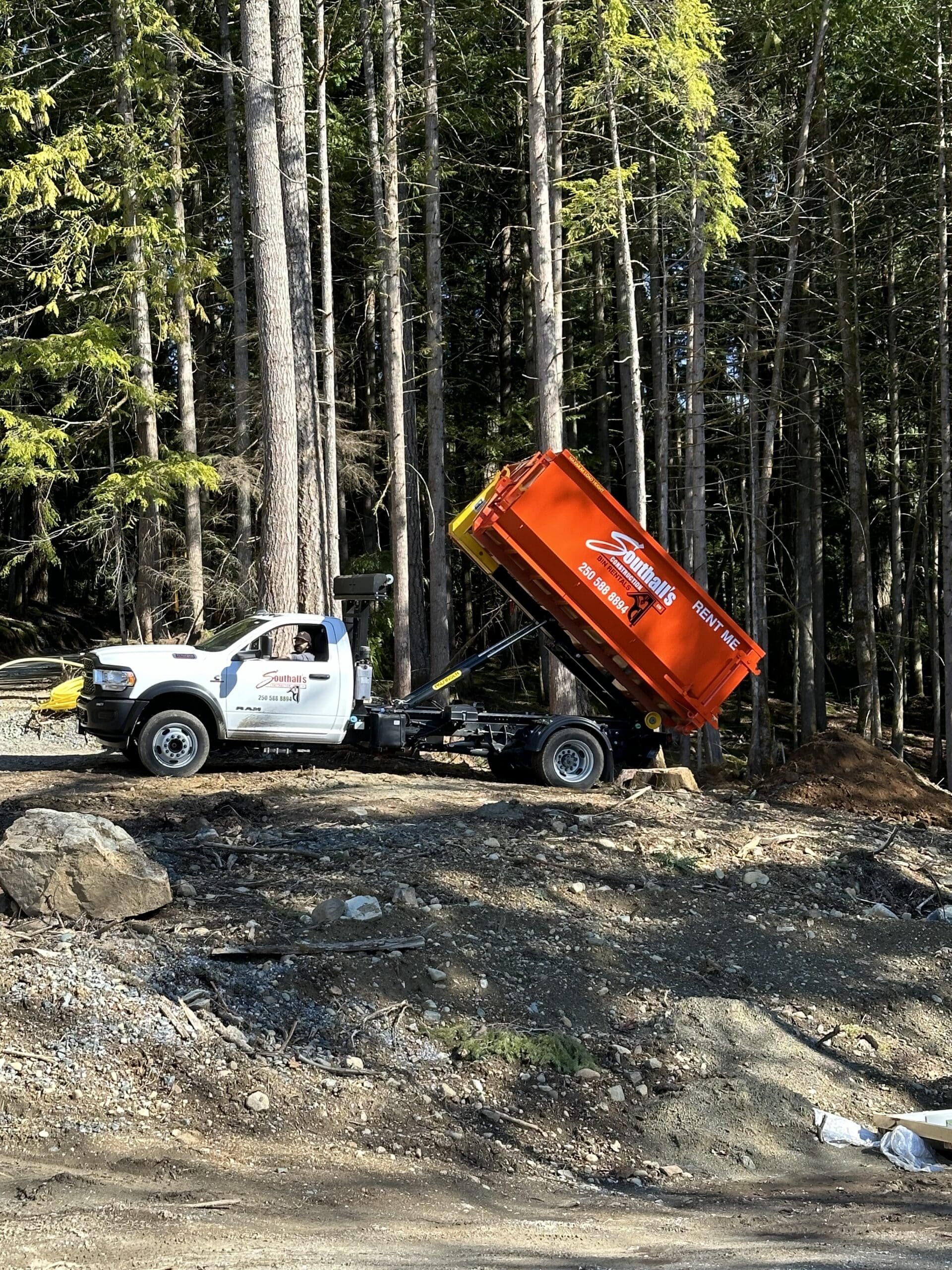 Southall’s Construction bin truck unloading an orange waste bin at a Shawnigan worksite surrounded by forest